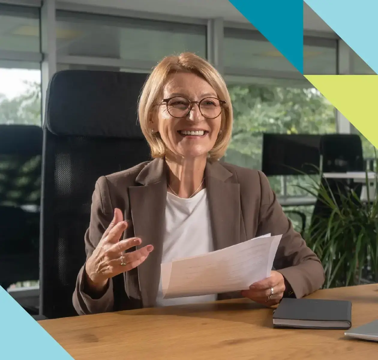 A woman with short blonde hair and glasses holds some business papers and smiles at someone off camera.