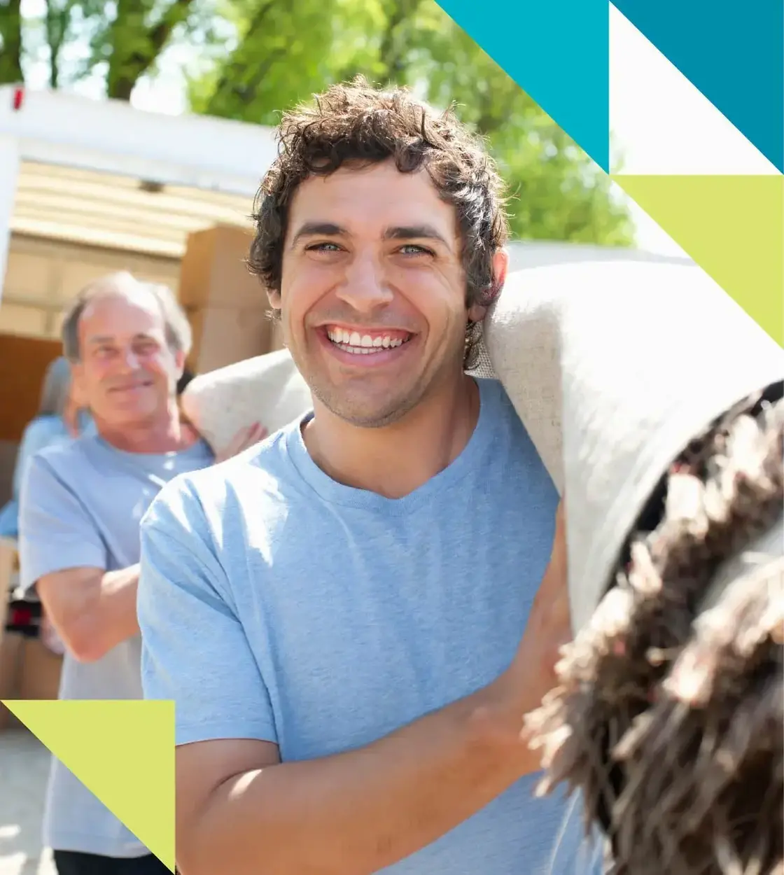 Two male movers in blue t-shirts smile as they haul out a large roll of carpet.