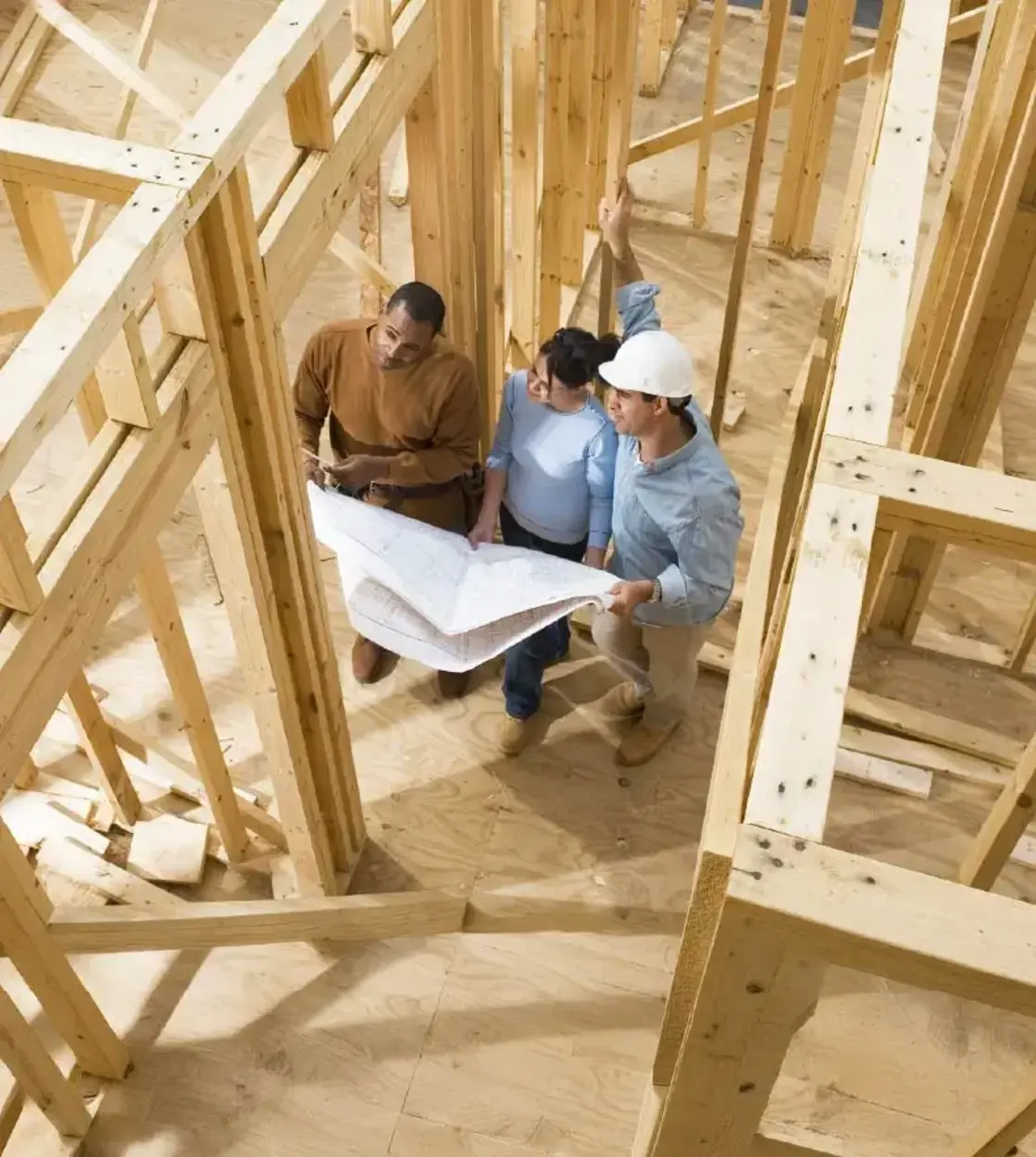 A husband and wife inspect their new home’s blueprints with the building contractor amid construction.
