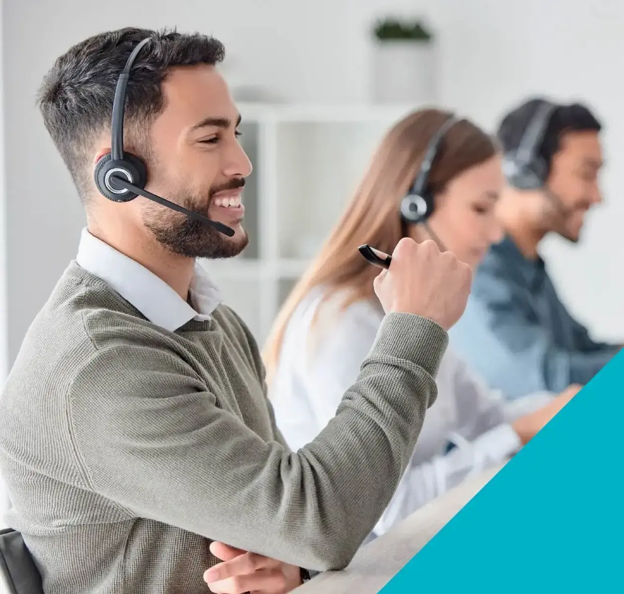 A young man with short hair wearing a headset smiles while working at a call centre.
