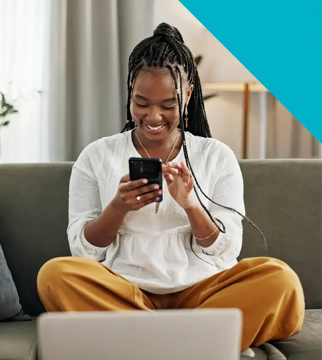 A woman in a white sweater smiles excitedly as she checks her mobile phone on the couch.