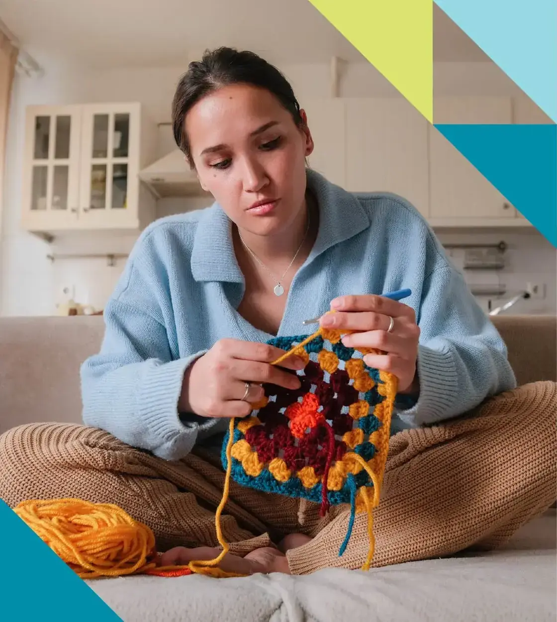 A young woman dressed in comfy attire works on a crochet project on her couch.