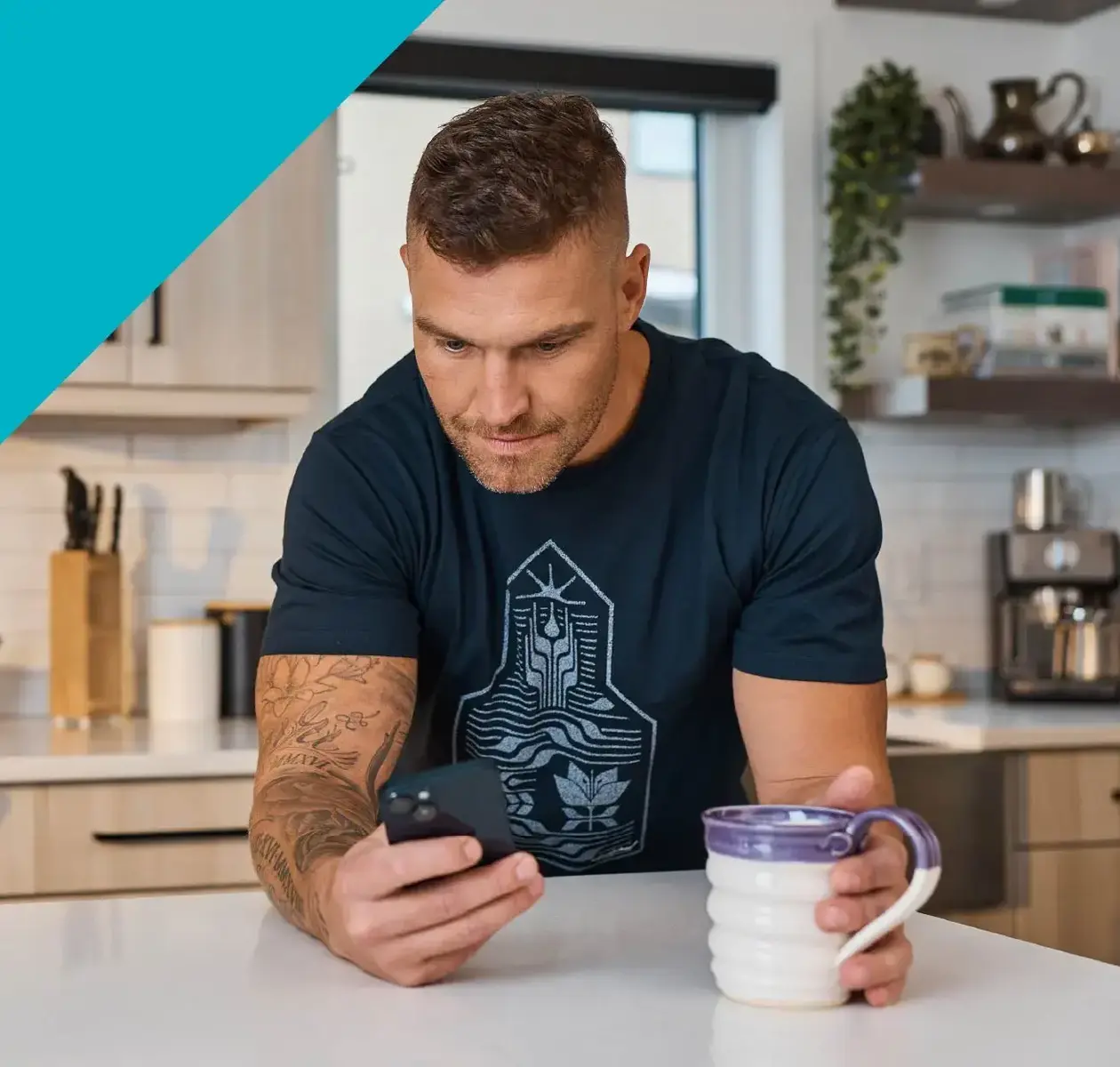 A young man wearing a printed t-shirt checks his phone while holding a cup of coffee.