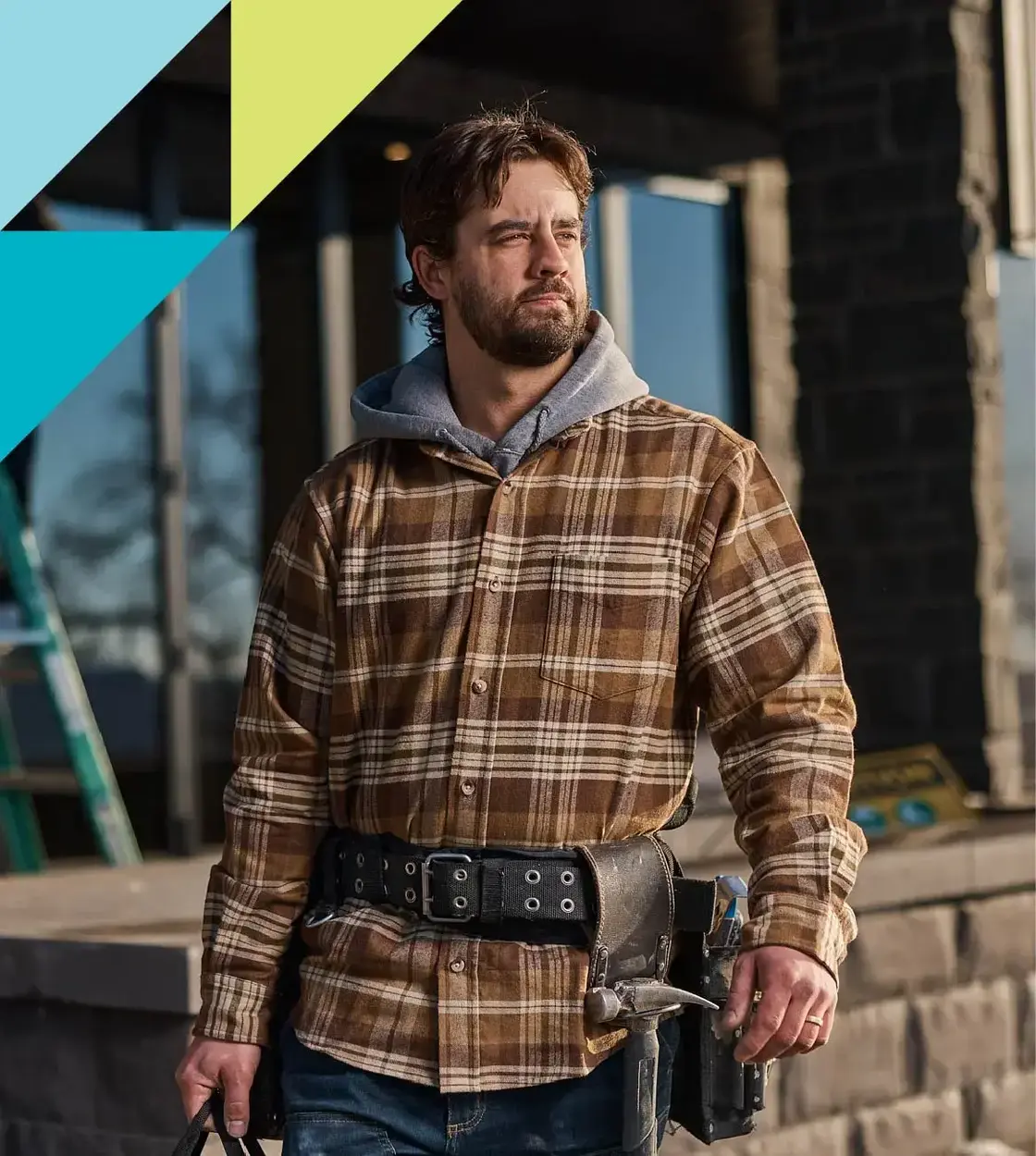 A bearded man in a flannel work jacket and tool belt looks off into the distance.