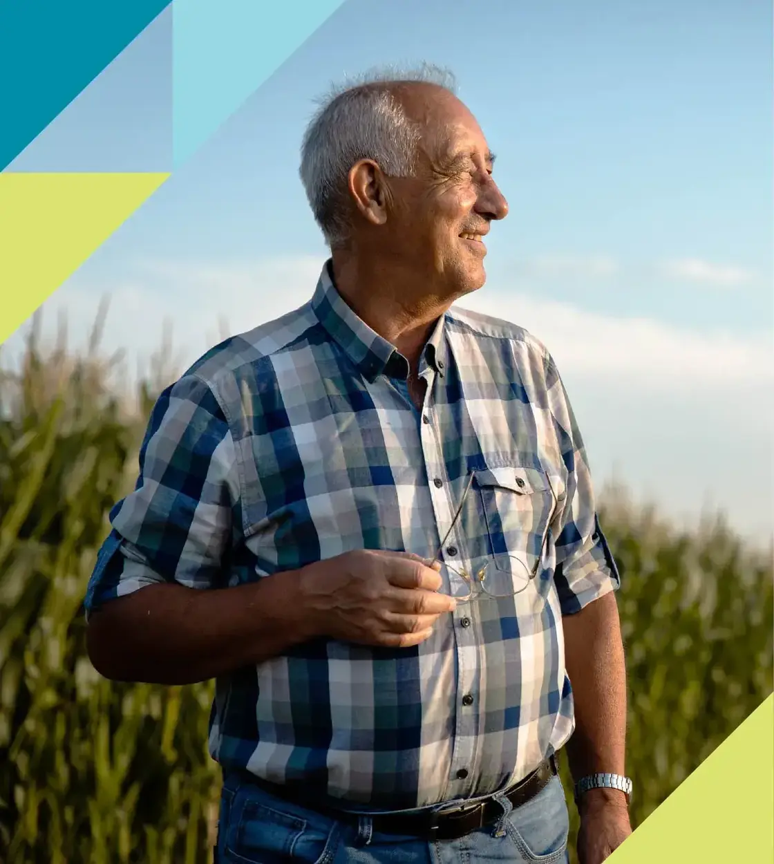 A man in a plaid shirt holds his glasses as he looks off into the distance with a contented smile.