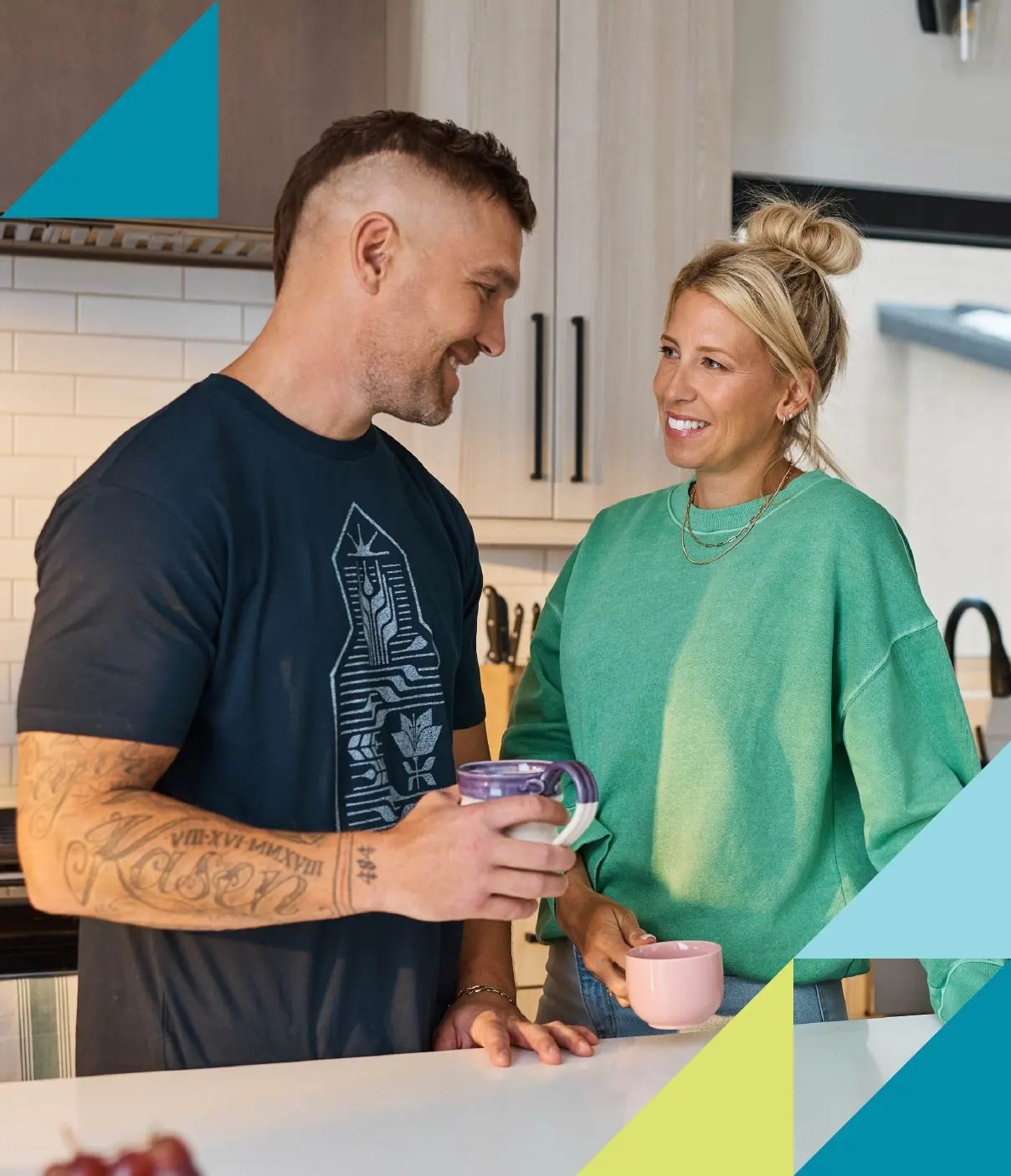 A young man and woman smile at each other as they enjoy a morning coffee in the kitchen.