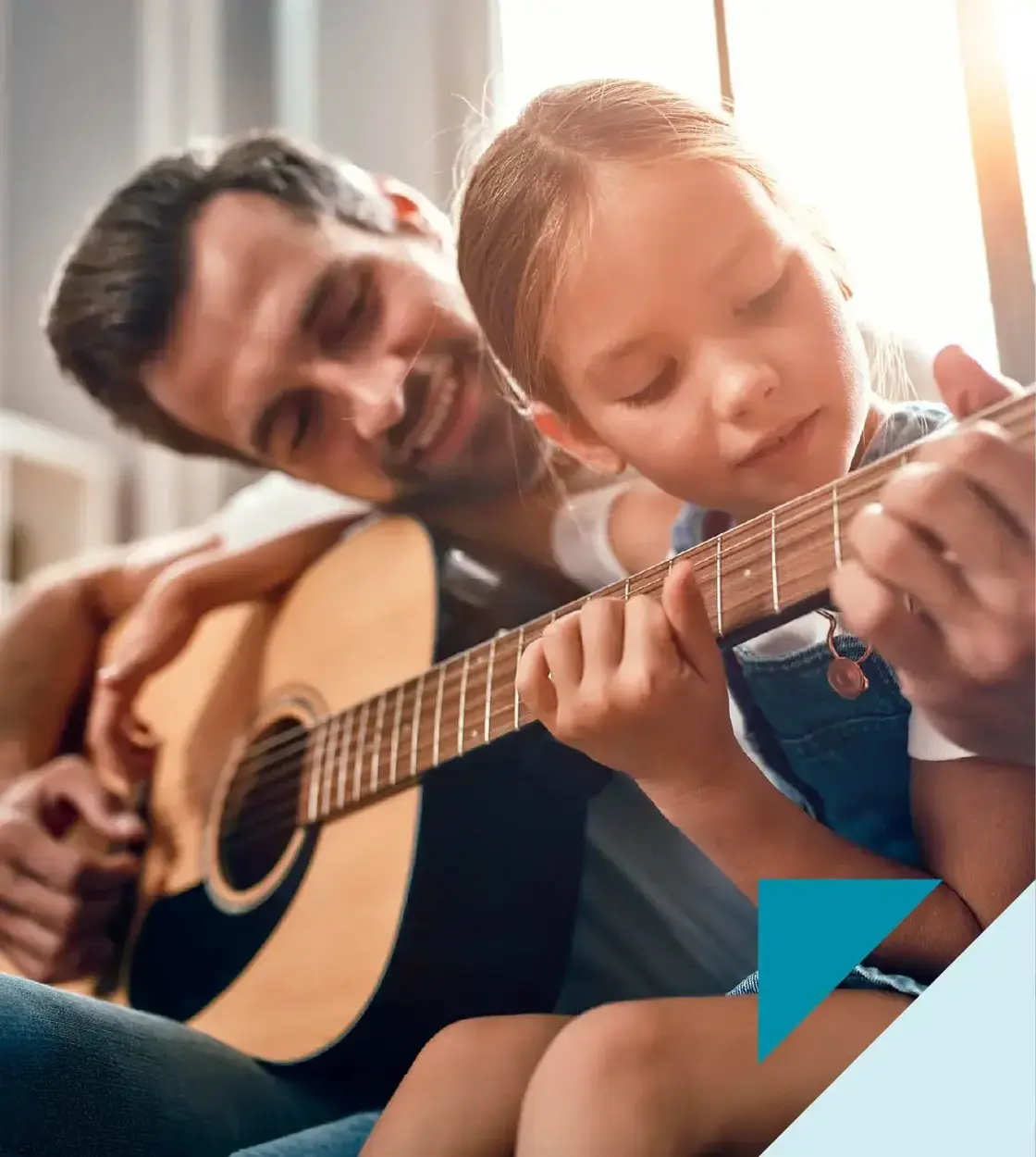 A father teaches his young daughter some chords on an acoustic guitar.