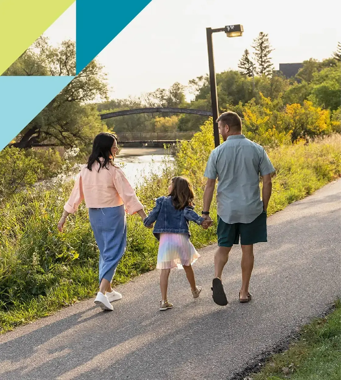 A mom and dad walk with their daughter along a path surrounded by lush vegetation.