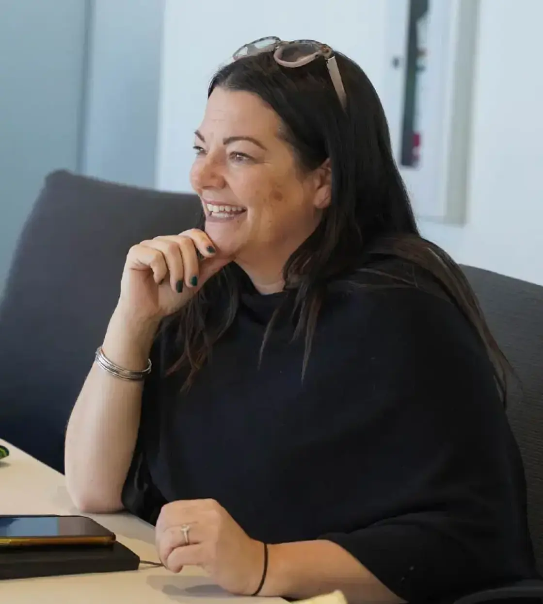 A woman in a black sweater with glasses on top of her head is smiling.
