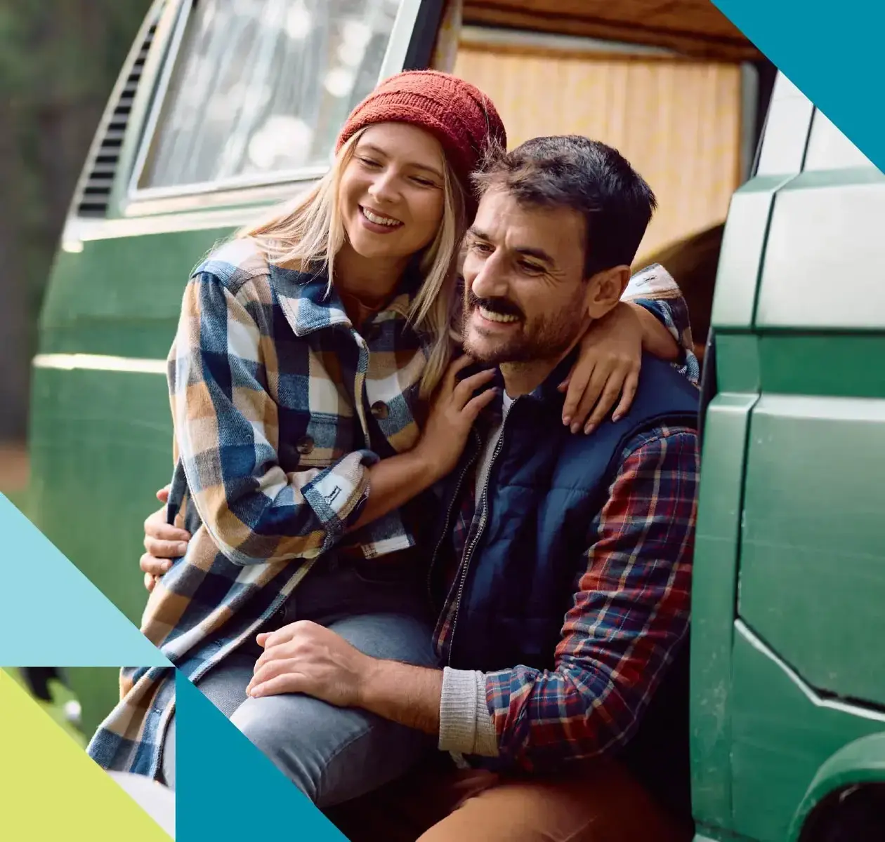 A man and woman each clad in flannel cheerily embrace one another outside their camper van.