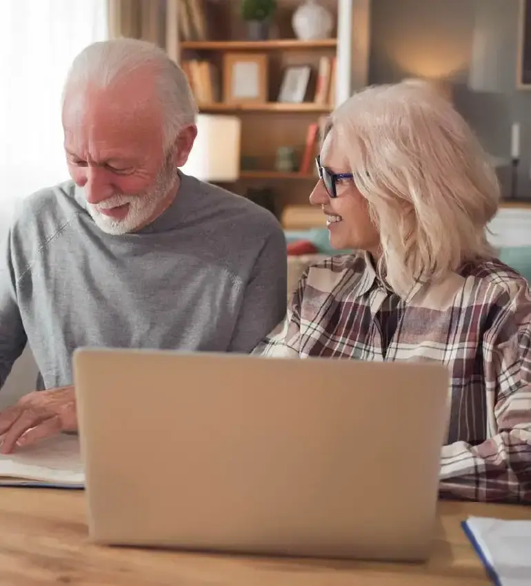A husband and wife in their golden years take care of some business using their laptop computer.