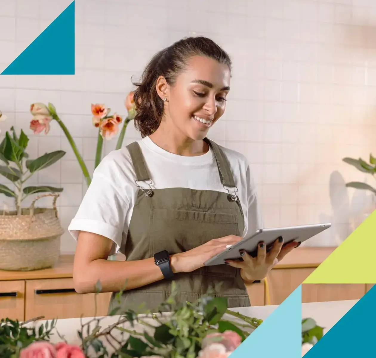 A female florist wearing an apron smiles while working on a tablet.