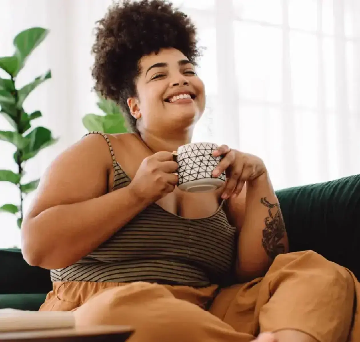 A woman dressed in comfy clothes relaxes on the couch with a nice cup of coffee.