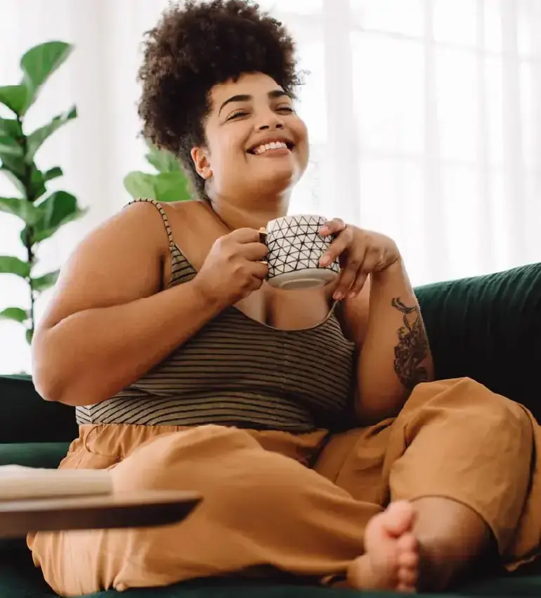 A woman dressed in comfy clothes relaxes on the couch with a nice cup of coffee.