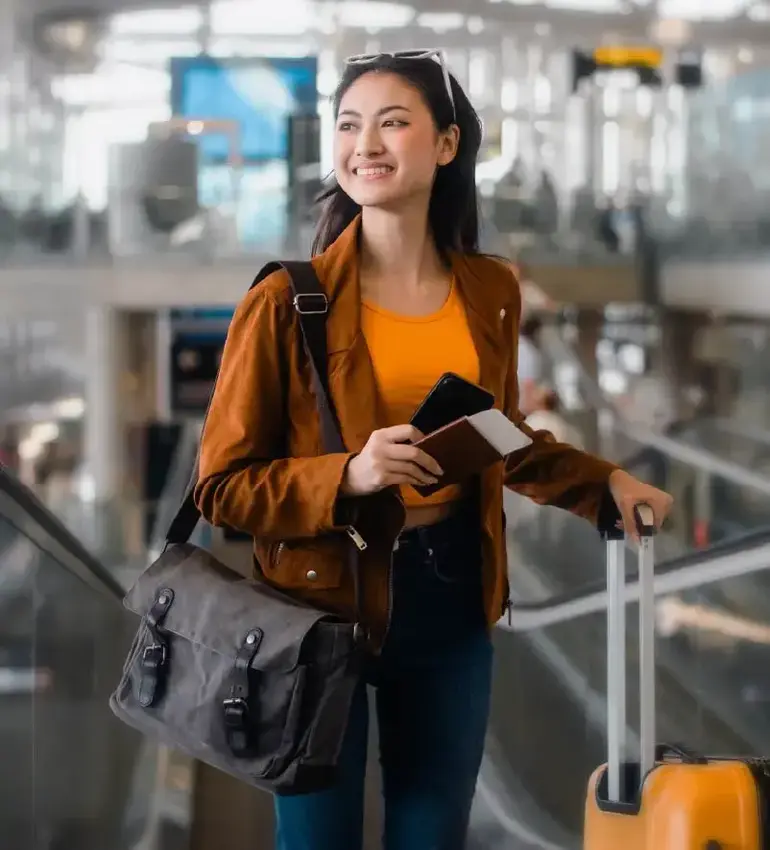 A young woman toting luggage beams with joy as she makes her way through the airport.
