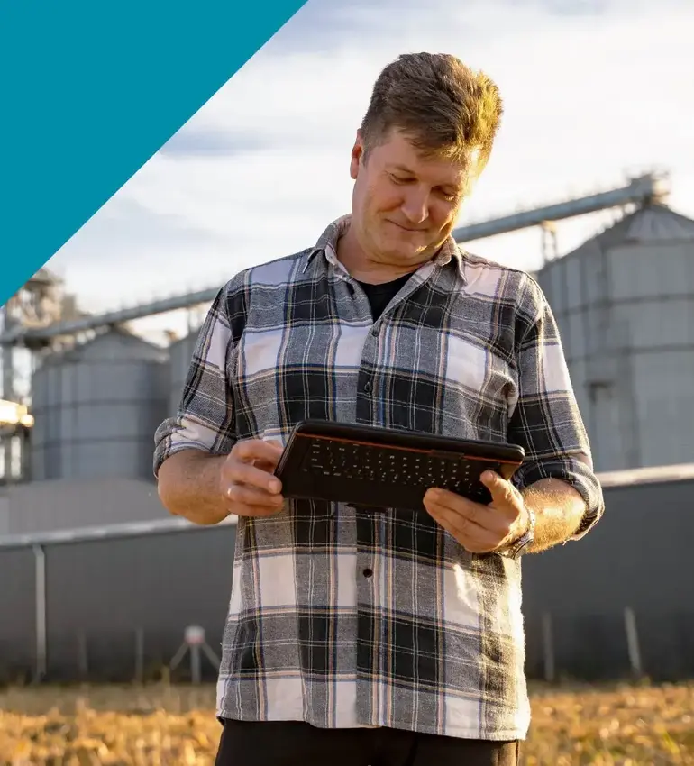 A man wearing a plaid shirt checks his tablet with storage bins behind him.