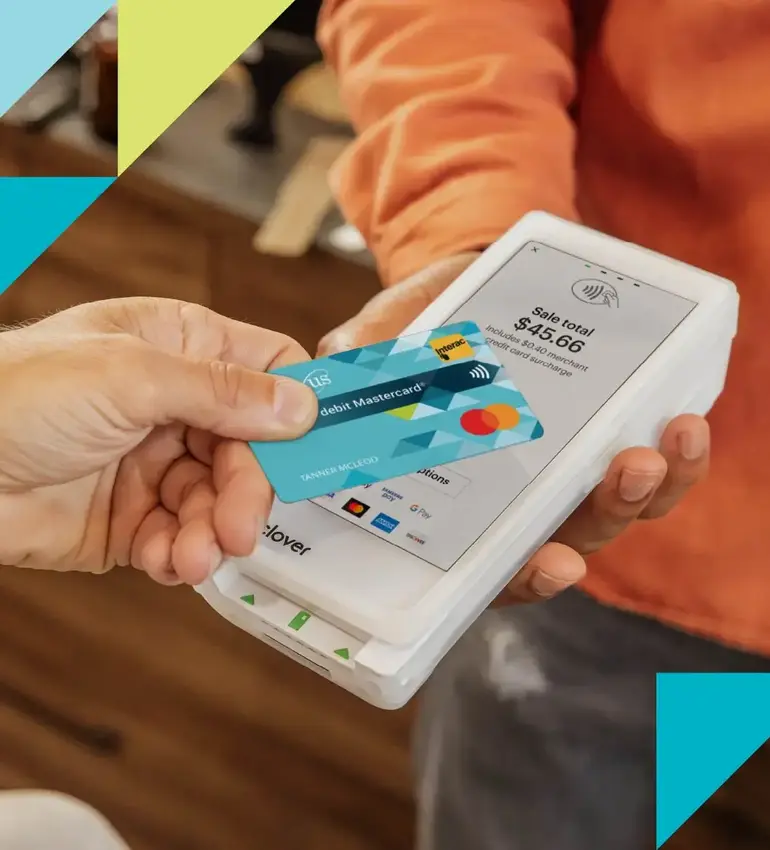 A hand holding a Conexus debit Mastercard taps a debit machine to complete a payment.
