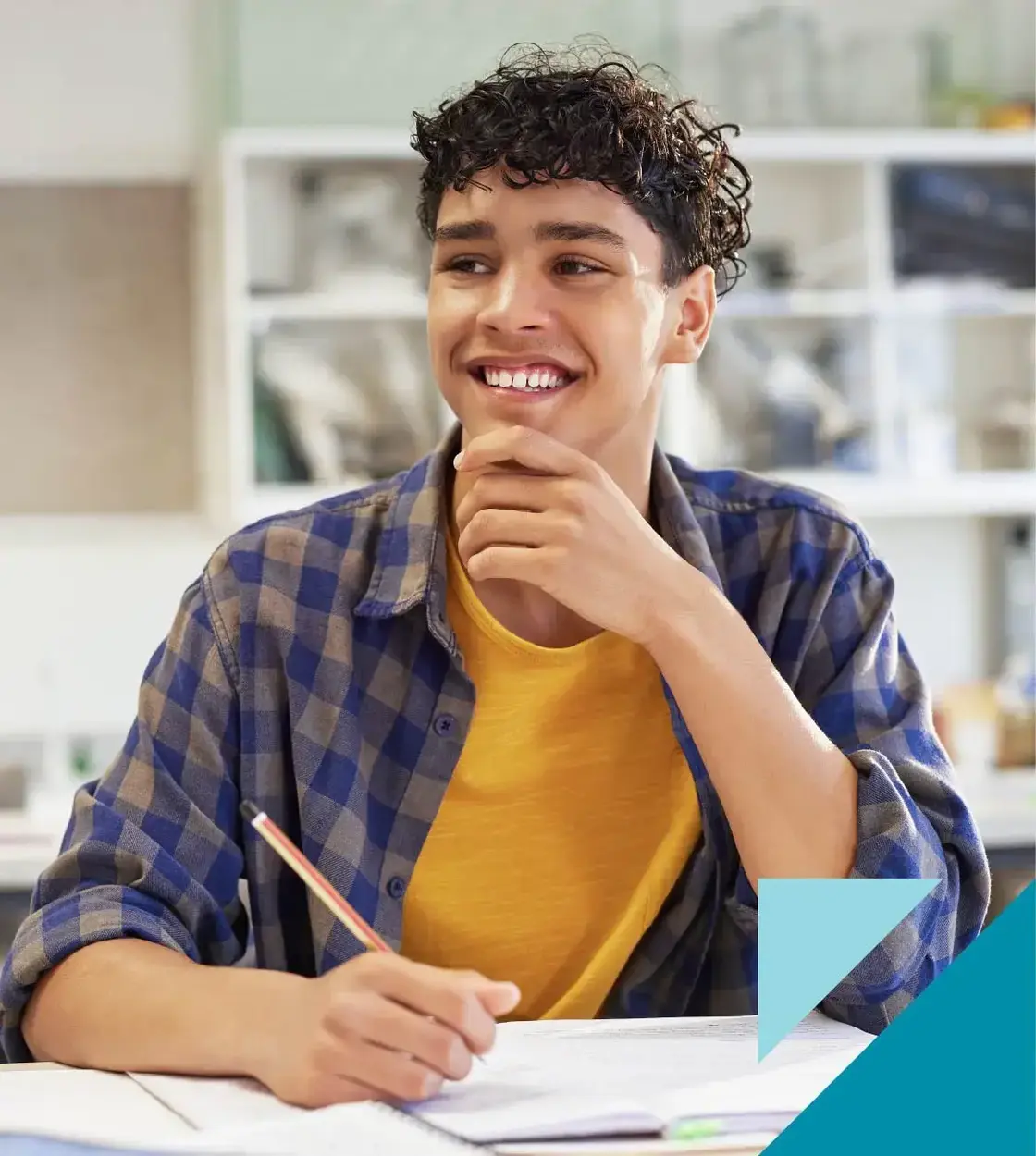 A teenage boy in flannel smiles while taking notes in class.