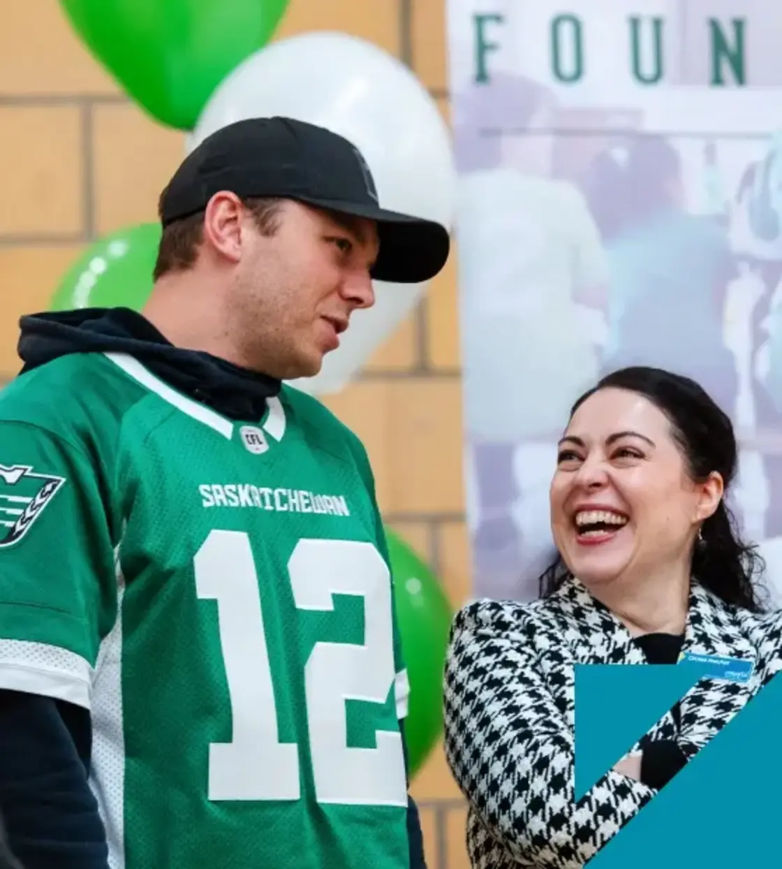 A female employee in a black and white checkered blazer laughs with a man in a Roughriders football jersey.