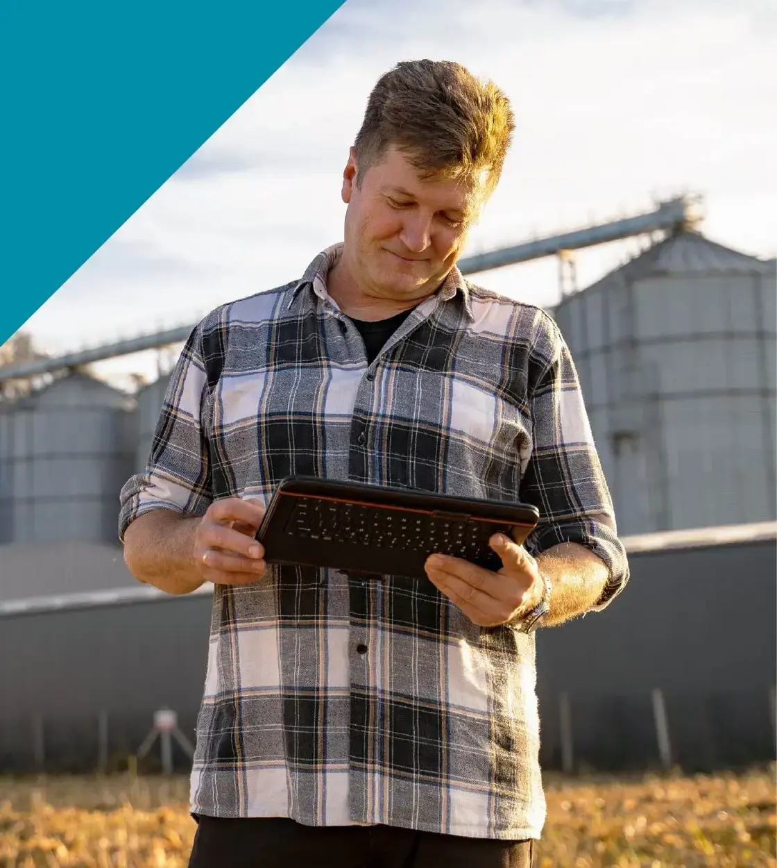 A man wearing a plaid shirt checks his tablet with storage bins behind him.