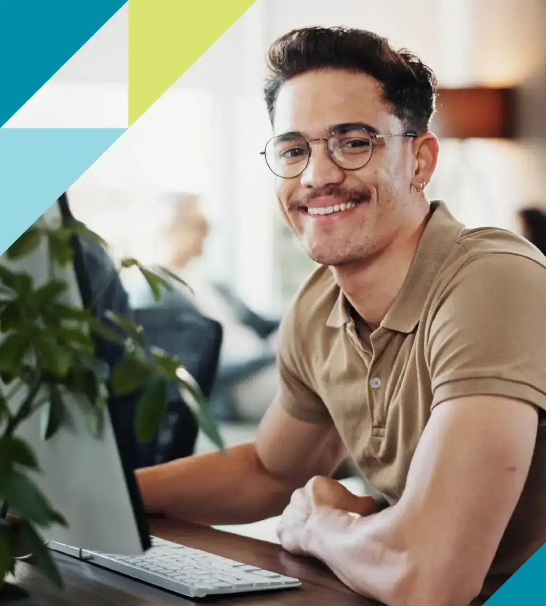 A man with glasses and moustache seated at his computer smiles at the camera.