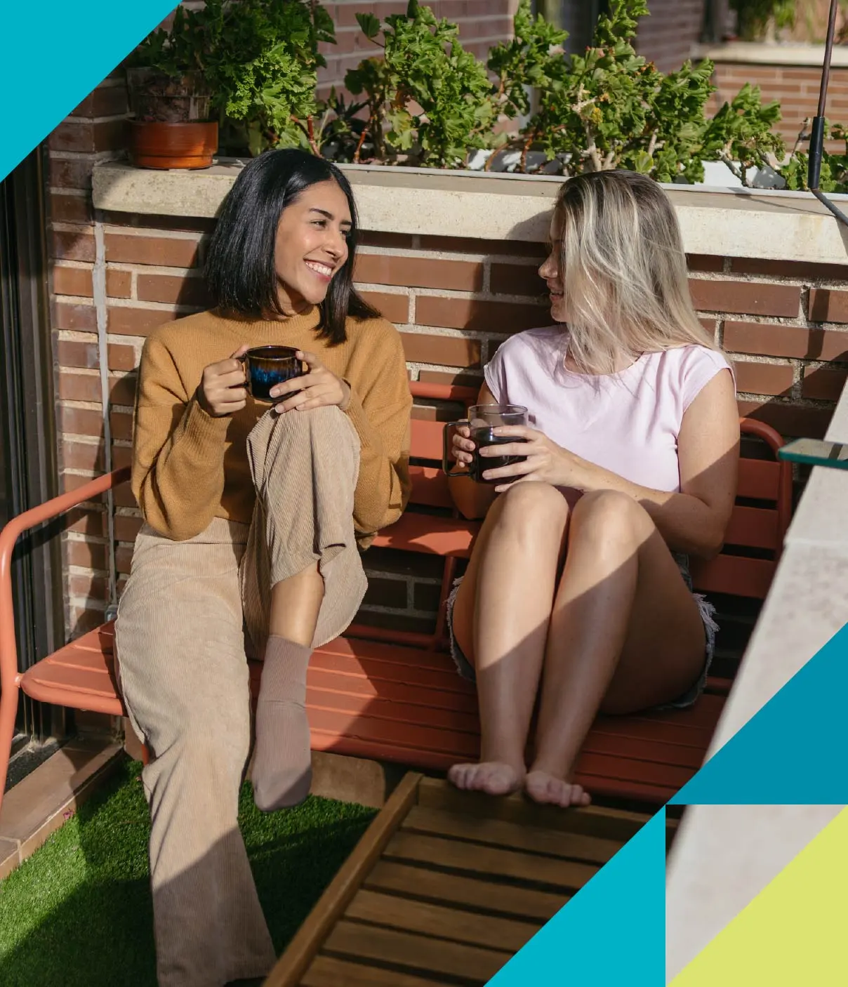 Two female friends sip coffee and engage in conversation while relaxing on a sunny patio.