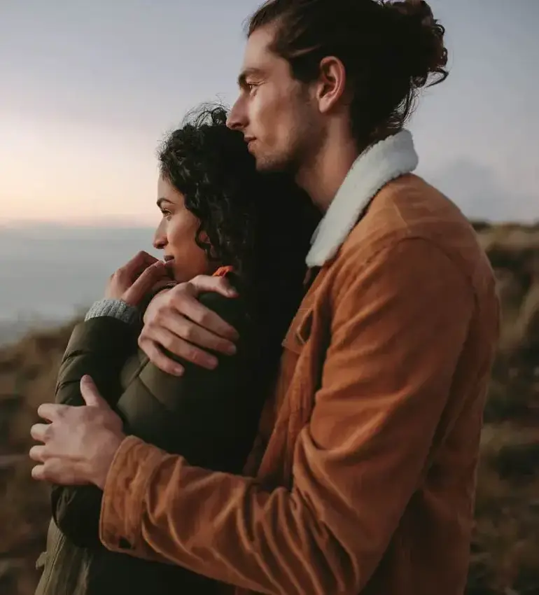 A man holds his girlfriend close as they peer out over a large body of water.