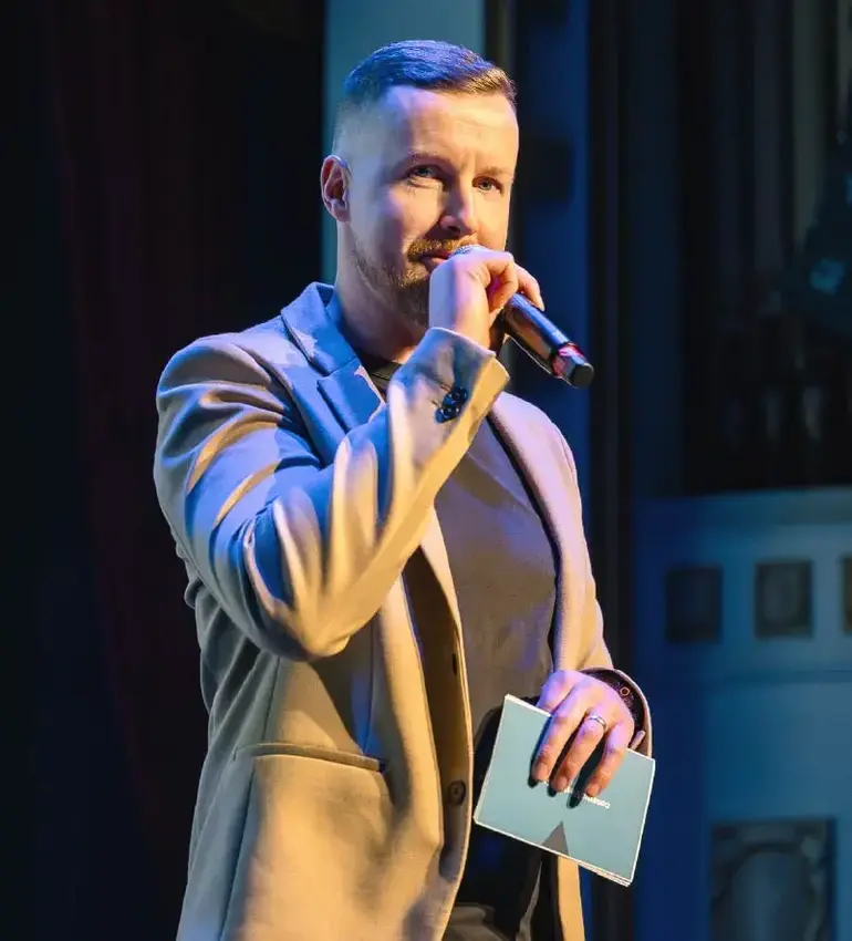 A man with short hair wearing a sport coat speaks into a microphone.