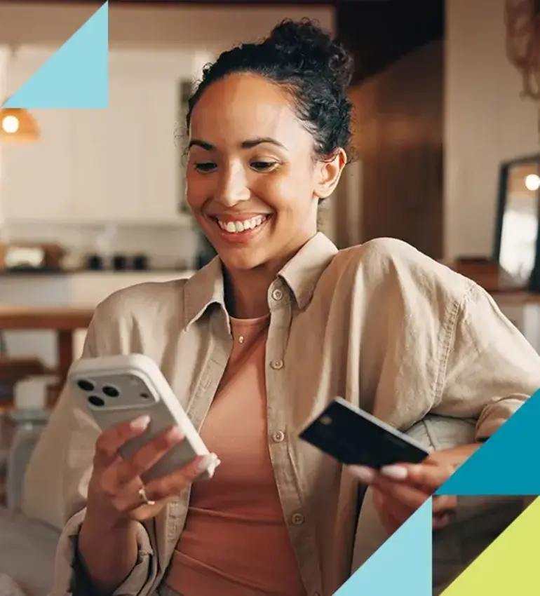 A young woman in a camel overshirt smiles as she checks her credit card balance using her mobile phone.