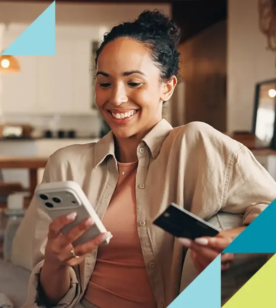 A young woman in a camel overshirt smiles as she checks her credit card balance using her mobile phone.
