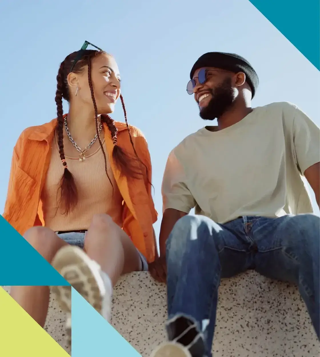 A woman in an orange shirt and pigtails smiles at a man next to her who’s wearing sunglasses and a toque.