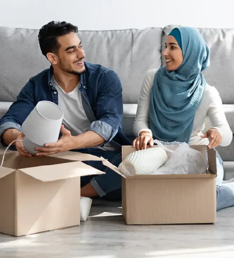 A pair of new homeowners trade smiles as they unpack home décor items.