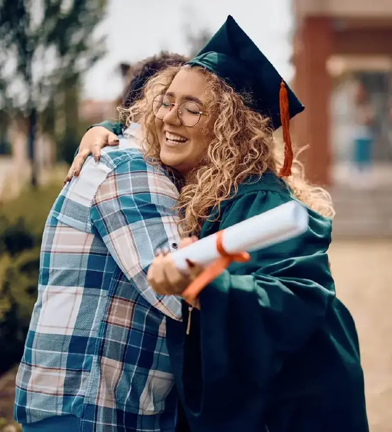 Donning a graduation cap and gown, a young woman receives a big hug on her day of celebration.