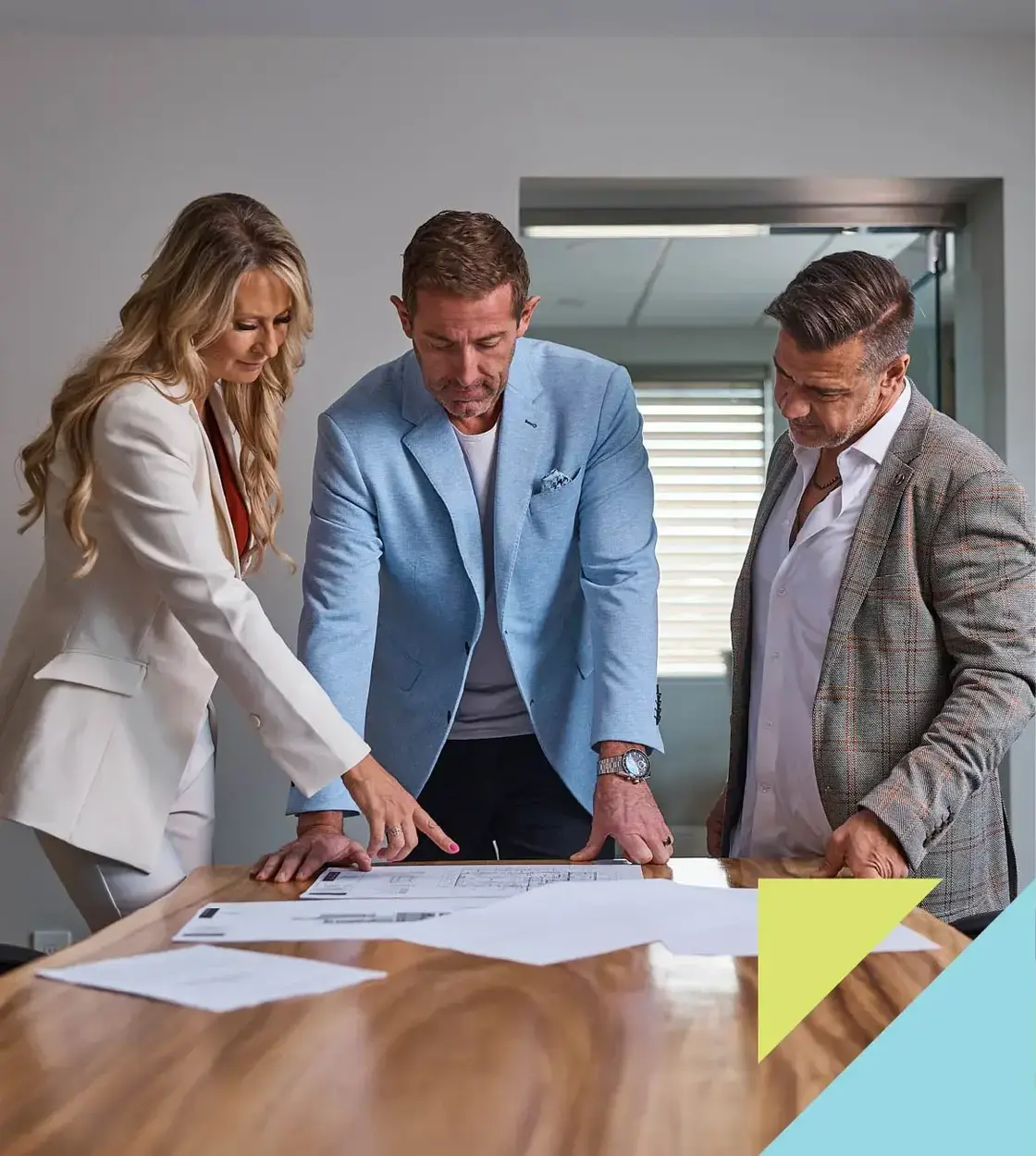 Three business professionals examine blueprints on a large table.
