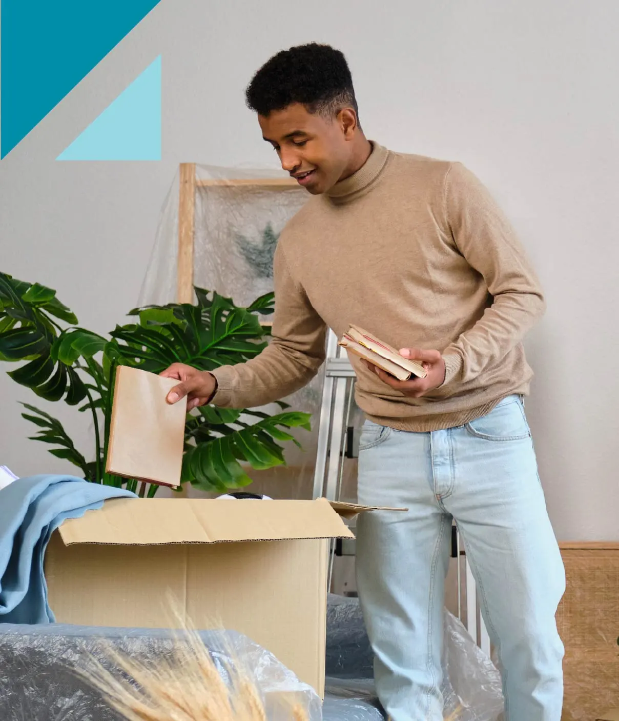A young man wearing a crewneck sweatshirt and jeans packs books into a cardboard box.