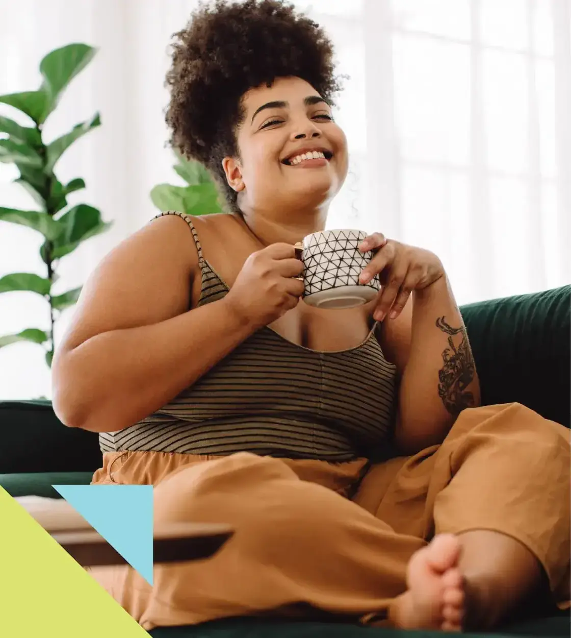 A woman dressed in comfy clothes relaxes on the couch with a nice cup of coffee.