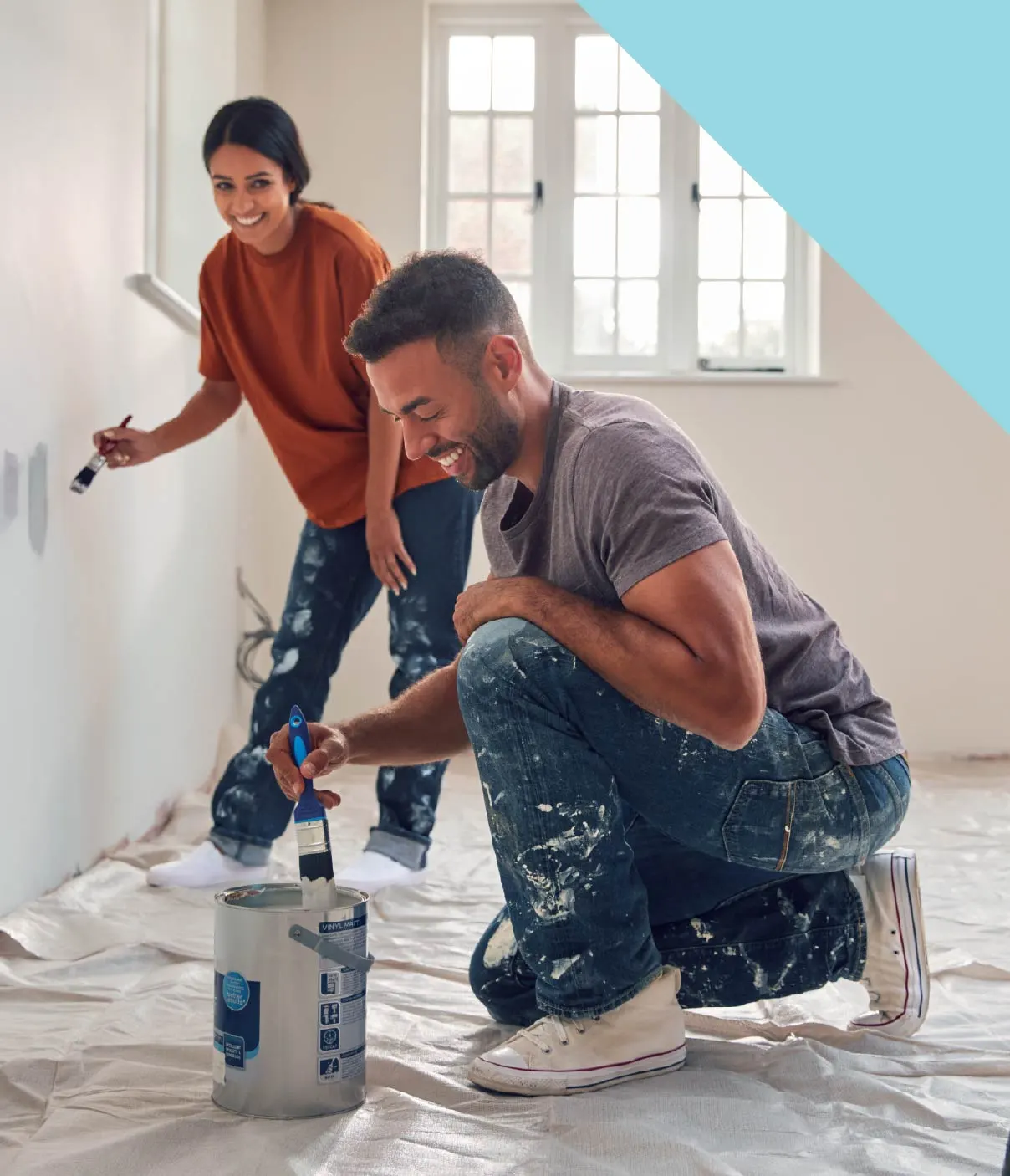 A young woman and man laugh as they paint a room in a house.