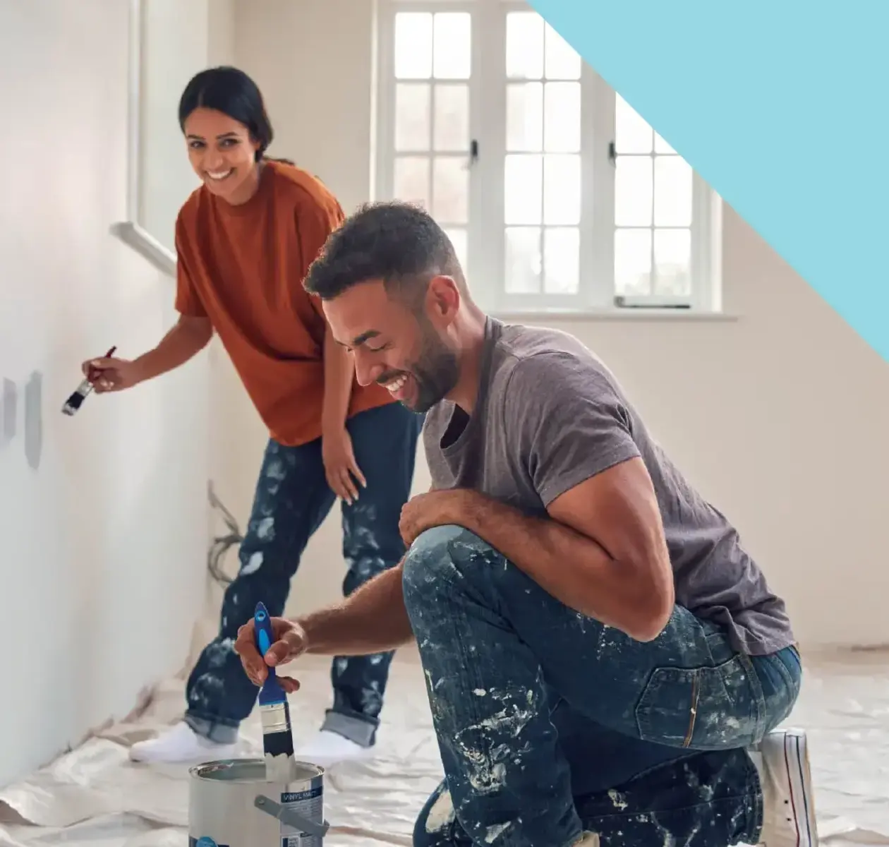 A young woman and man laugh as they paint a room in a house.