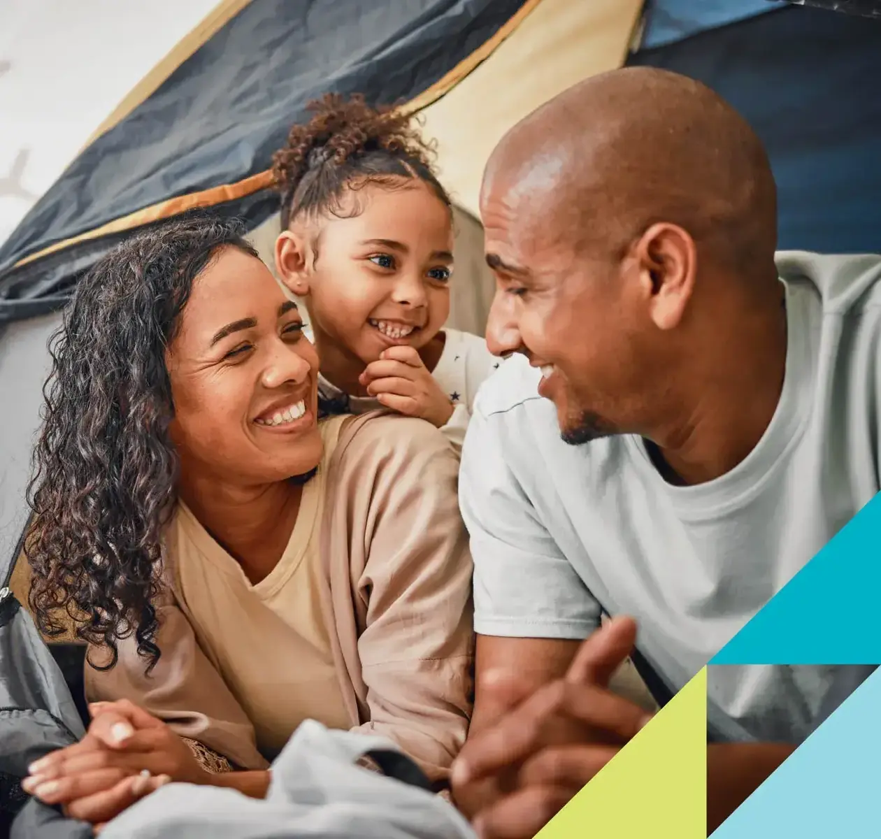 A mom, dad and daughter smile at one another as they gear up for a sleepover in a tent.