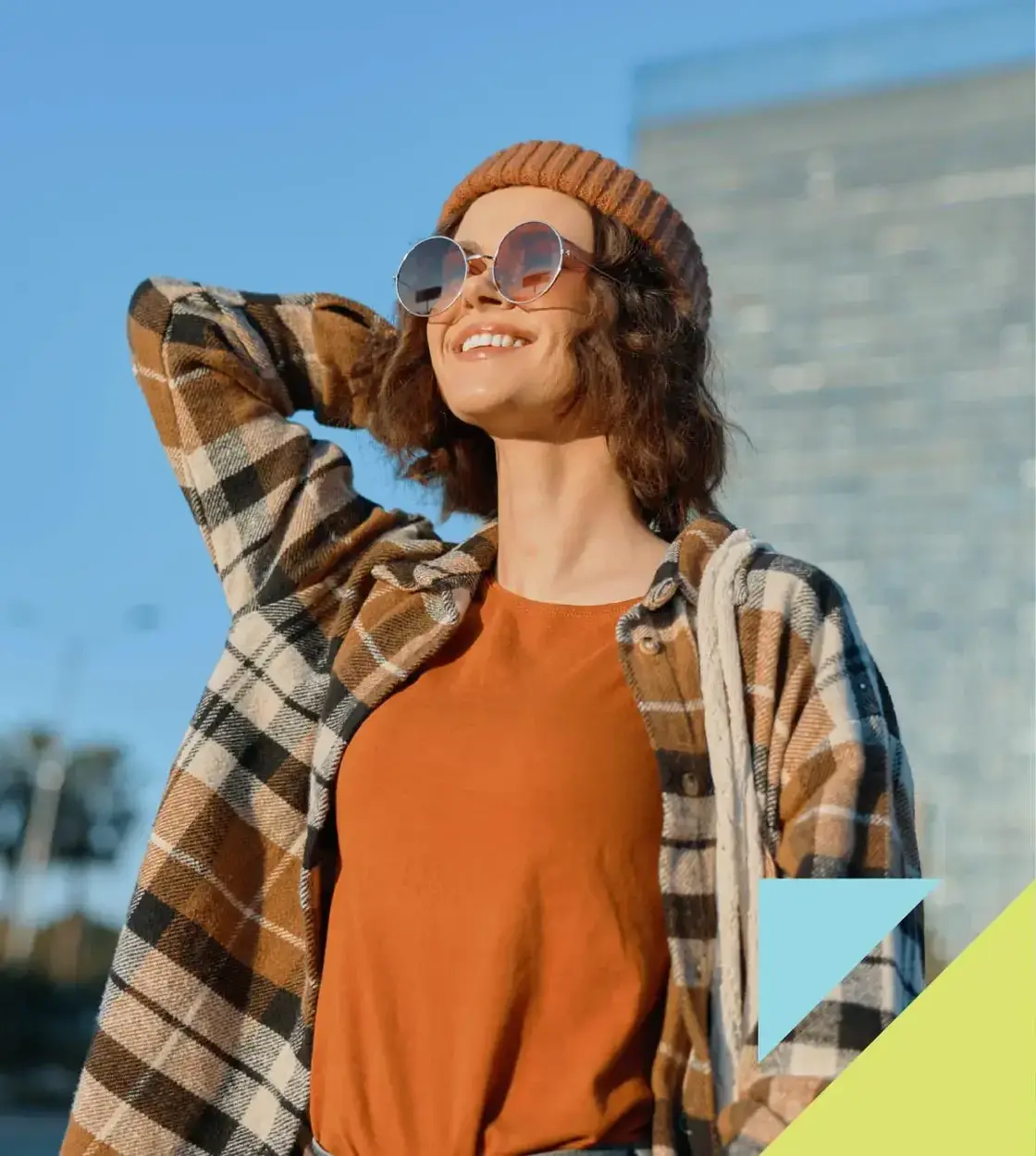 A young woman wearing flannel, sunglasses and a toque smiles into the autumn sun.