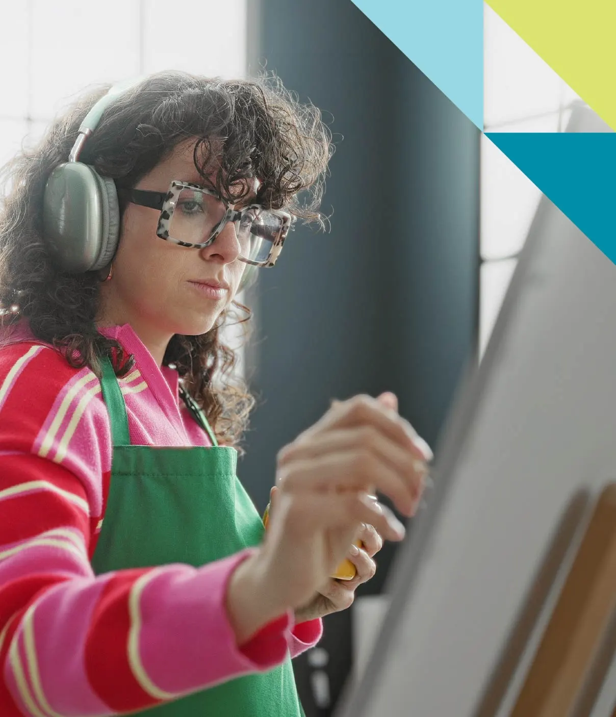 A young woman wearing glasses and headphones is focused on her latest paint creation.