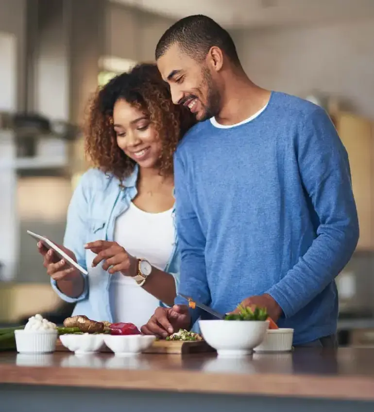 A man and woman prepare a meal at home by following an online recipe via mobile phone. 