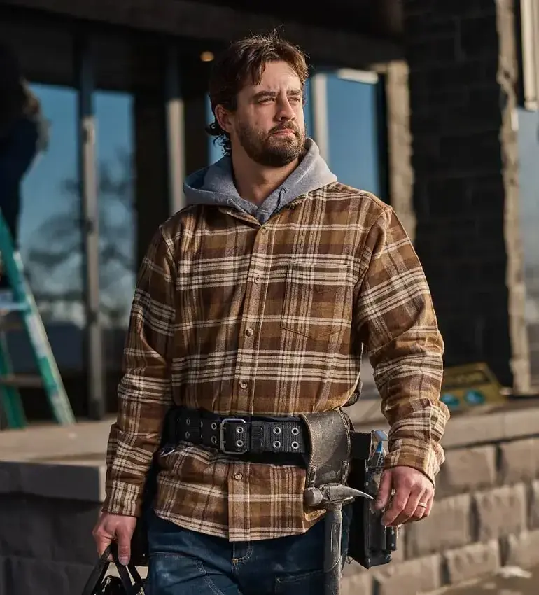 A bearded man in a flannel work jacket and tool belt looks off into the distance.