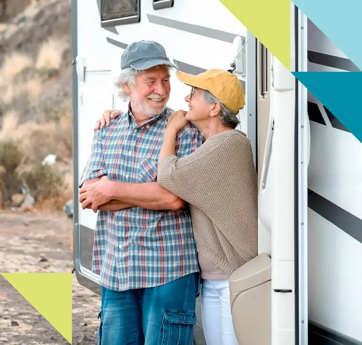 A mature couple in comfortable camping gear smile at each other next to their recreation vehicle.