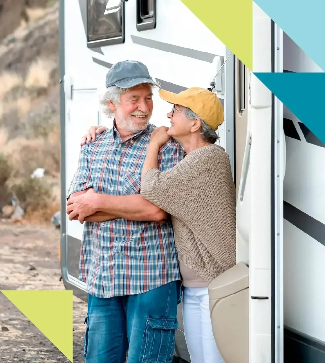 A mature couple in comfortable camping gear smile at each other next to their recreation vehicle.