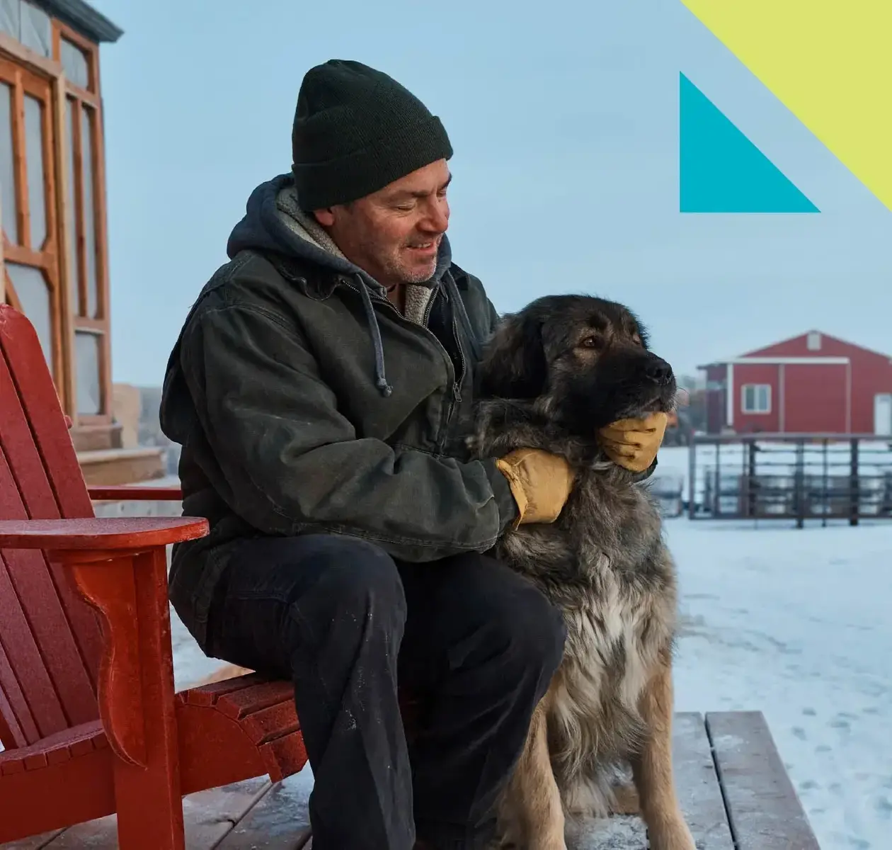 A man dressed for winter sits on his farm deck while scratching his lovable dog.