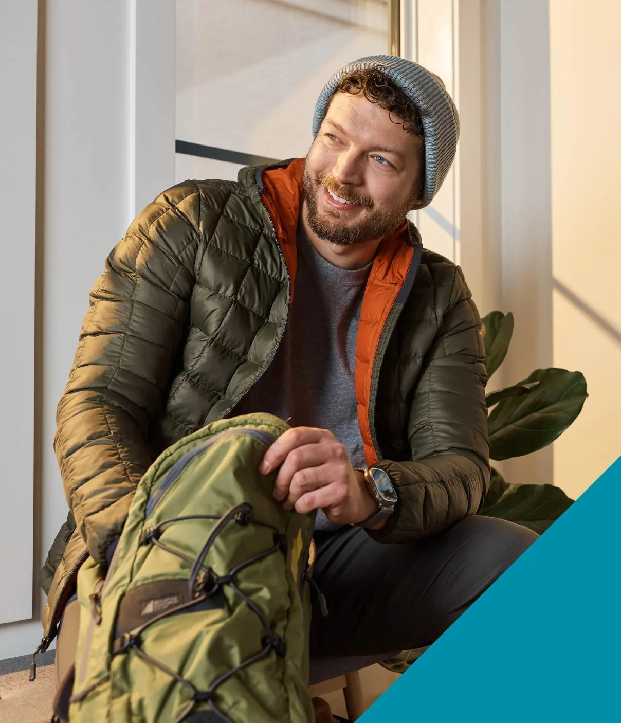 A young man wearing a puffy coat and grey toque smiles while he fills his backpack.