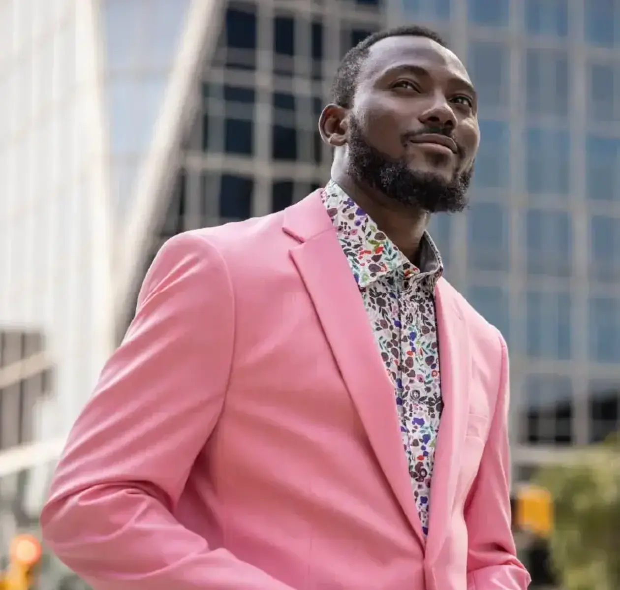 A man in a pink blazer and paisley shirt contentedly looks off into the distance.