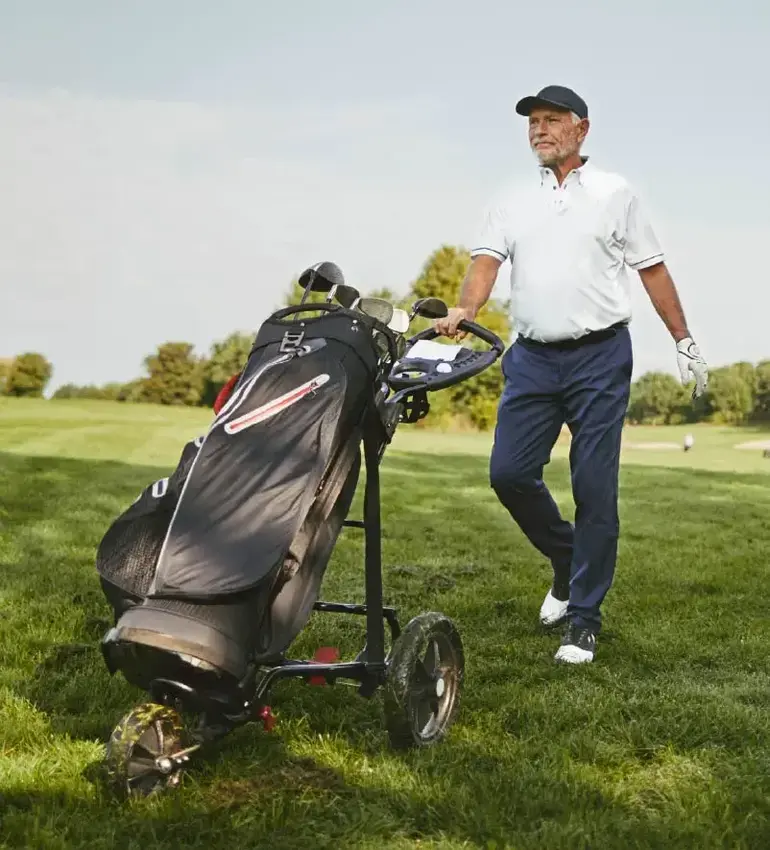 A man on a golf course walks towards his ball with his clubs in tow.