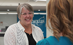 A female employee with grey hair and glasses is smiling at a member. 